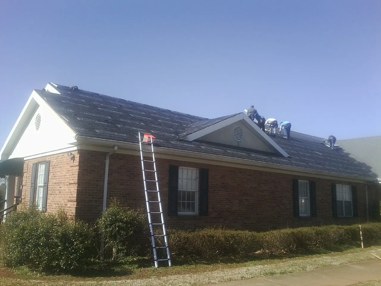 Crew tearing shingles off a brick ranch roof with a ladder set — Emergency Roof Repair work by our crew in Osage Beach