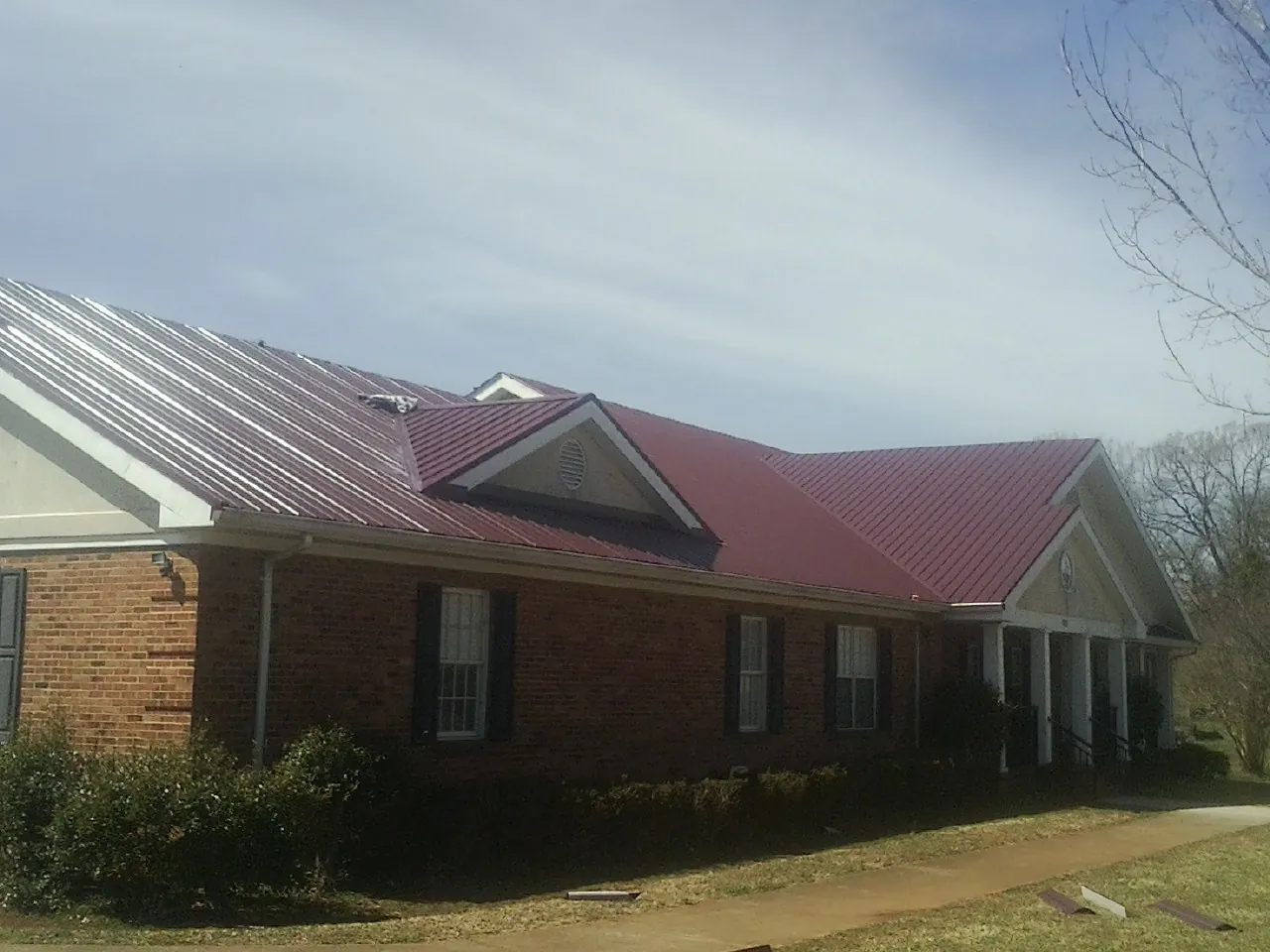 Red metal roof with gabled entries on a long brick building, from a Hail Damage Roof Repair job in Osage Beach