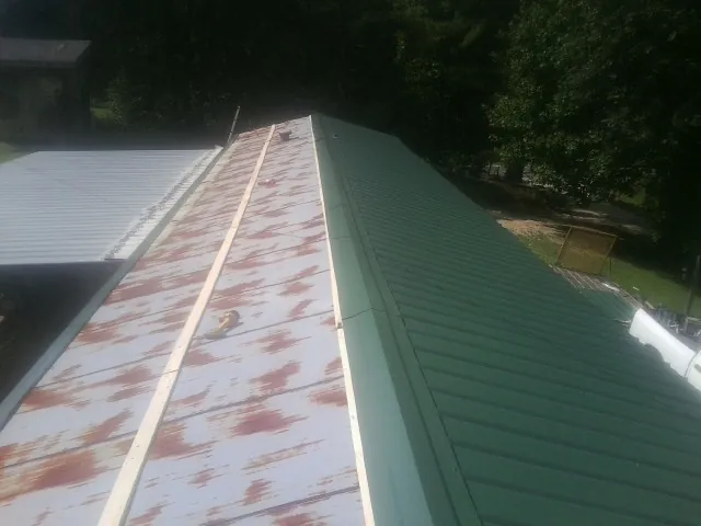 Old rusted panels beside newly installed green metal roofing — Wind Damage Roof Repair by Roofing Brothers in Osage Beach