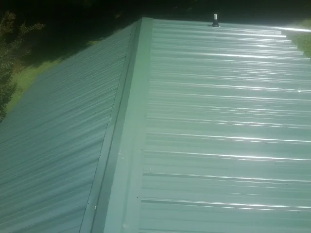 New green metal panels meeting at the ridge of a roof — Flat Roof Repair work by our crew in Osage Beach