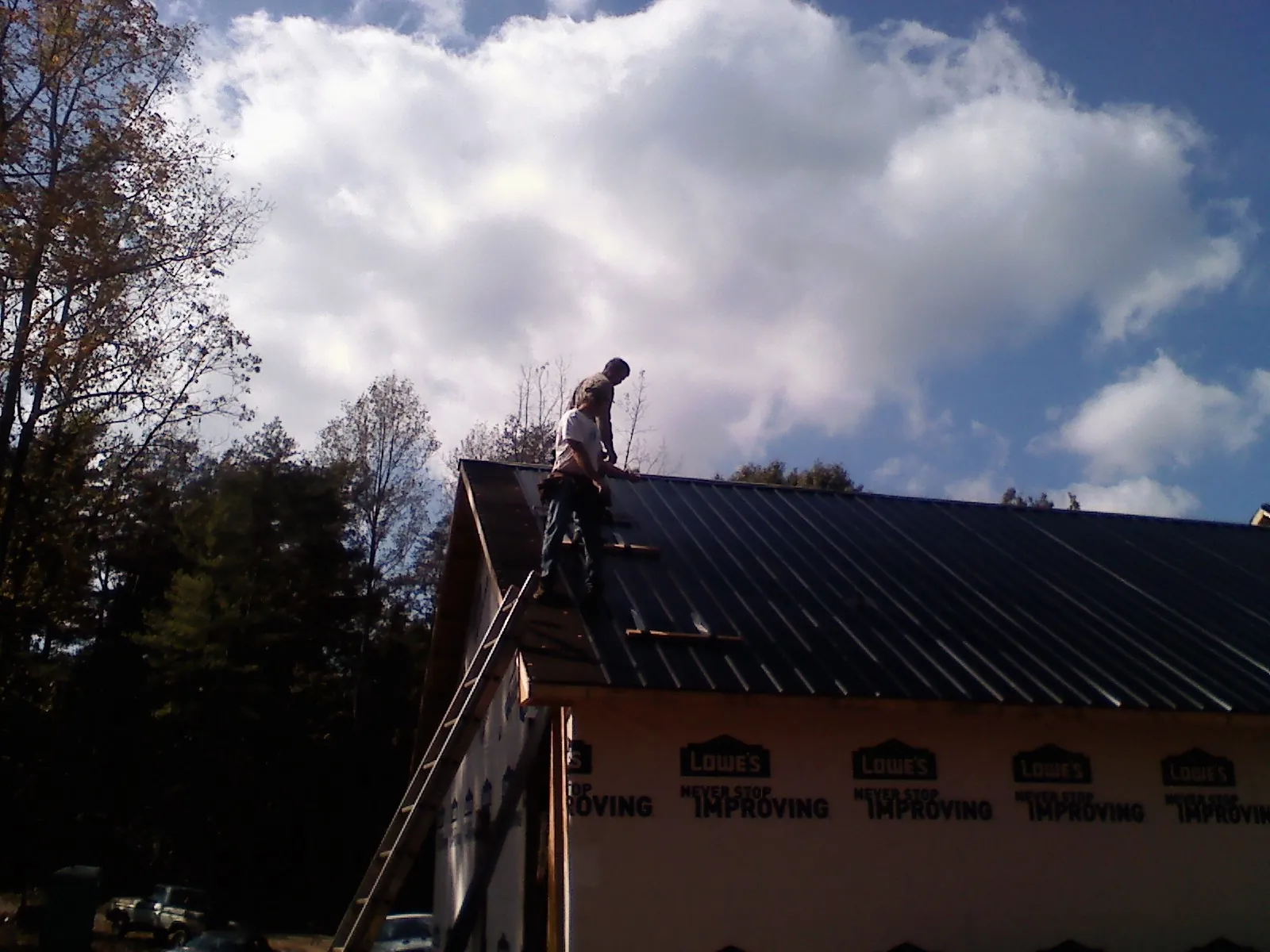 Roofer fastening dark metal panels high against a cloudy sky, from a Roof Inspection job in Osage Beach