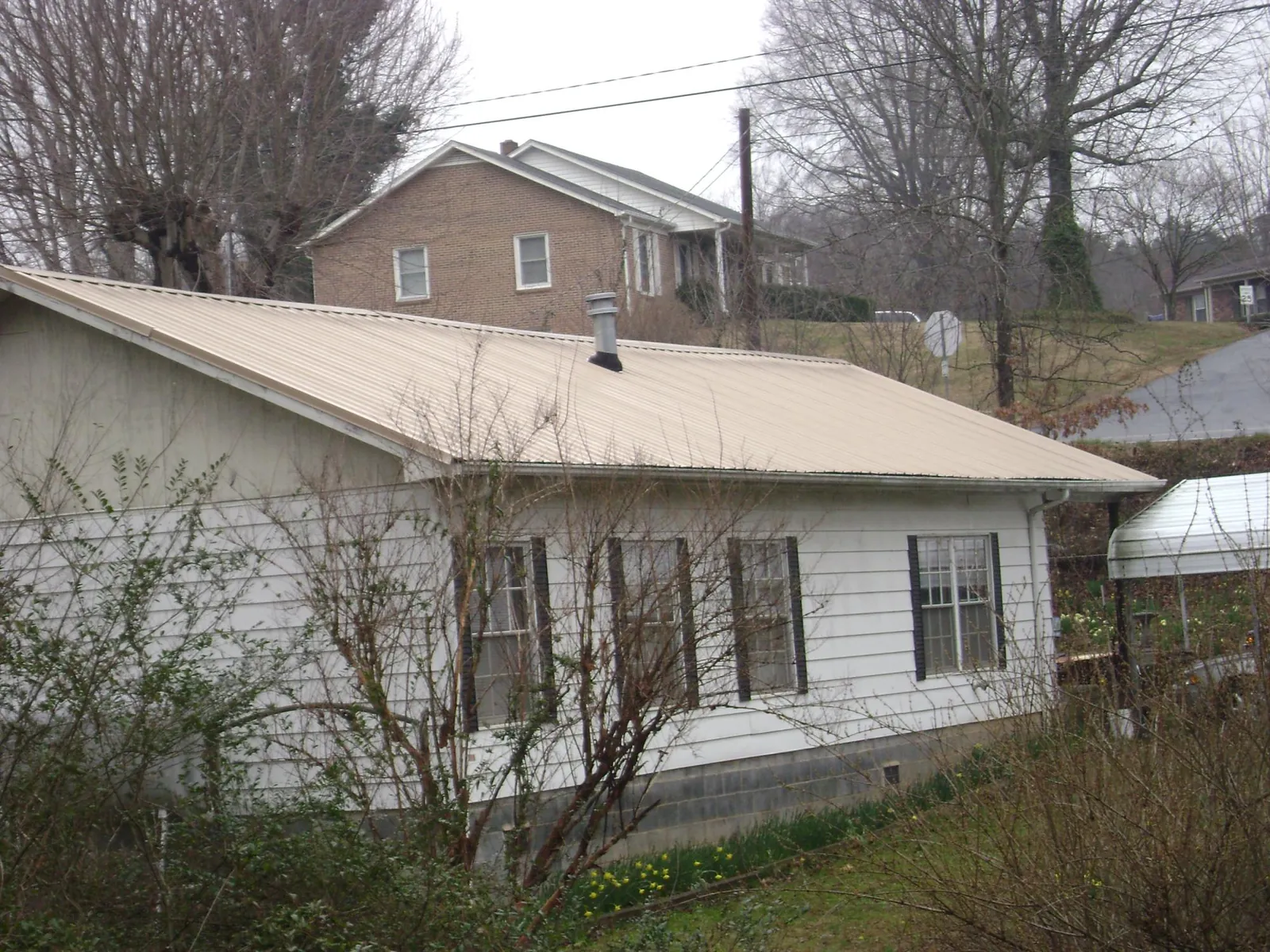 Tan metal roof on a white sided house set into a hillside — Commercial Roofing by Roofing Brothers in Osage Beach